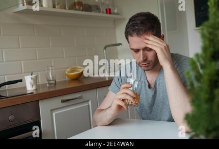 Müde Mann mit Glas Whiskey in der Küche sitzen. Stockfoto