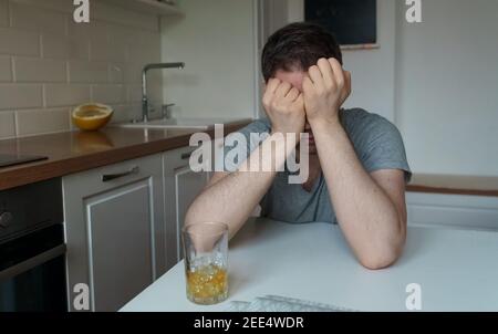 Müde Mann mit Glas Whiskey in der Küche sitzen. Stockfoto