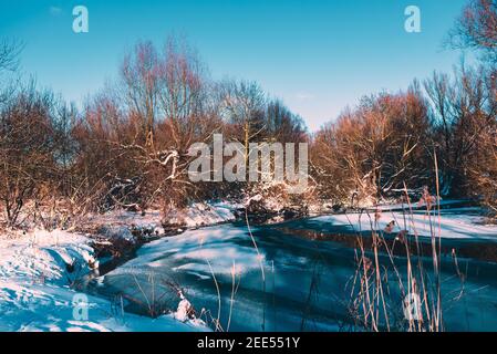 Eisiger Fluss in der Abendsonne, der die Bäume am Ufer beleuchtet Stockfoto