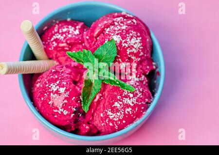 Himbeer-Eis in blauer Schale auf Steintisch, verziert mit mehreren Minzblättern und Waffeleisen. Stockfoto