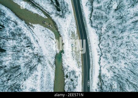 Luftaufnahme von oben auf Straße und Fluss in Bergschlucht in verschneiten Wintertag, Drohne Sicht. Stockfoto