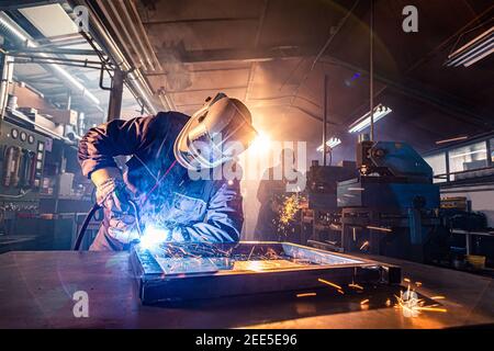 Die beiden Handwerker beim Schweißen und Schleifen an ihrem Arbeitsplatz in der Werkstatt, während die Funken um sie herum "fliegen", tragen sie einen schützenden HE Stockfoto