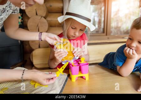 Niedlich liebenswert junge kaukasische kleine Mädchen Kind sitzt am Tisch Haushof und Spaß machen mit Mama hausgemachten Fruchtpüree Eis. Junge glückliches Kind Stockfoto