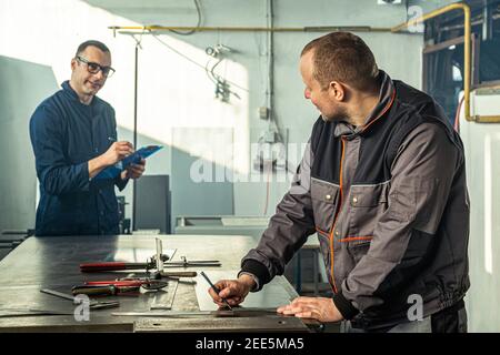 Ein Kinnschmied skizziert in der Werkstatt und er berät sich mit einem Kollegen Ingenieur, der Notizen macht. Stockfoto