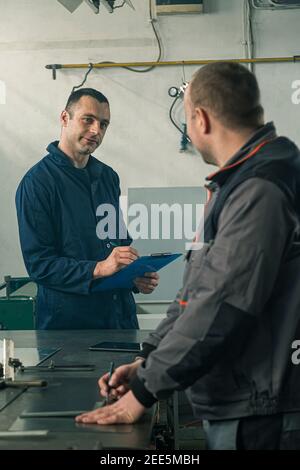 Ein Kinnschmied skizziert in der Werkstatt und er berät sich mit einem Kollegen Ingenieur, der Notizen macht. Stockfoto