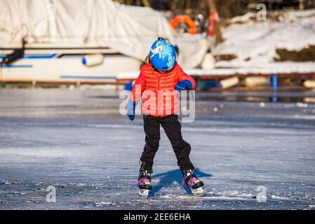 Prag, Tschechische republik - 14. Februar 2021. Junges Mädchen in roter Jacke mit blauem Helm lernen Eislaufen auf gefrorenen Fluss Stockfoto