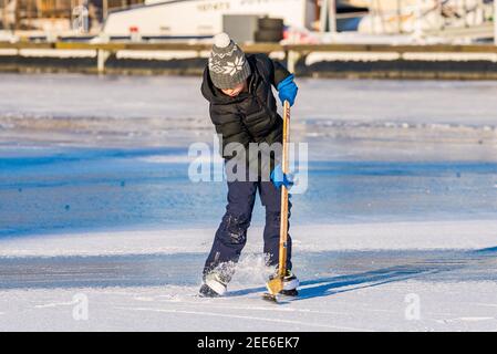 Prag, Tschechische republik - 14. Februar 2021. Junge versucht, den Puck mit Eishockey-Stick auf gefrorenen Fluss schlagen Stockfoto