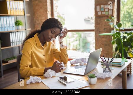 Foto-Porträt von afroamerikanischen Frau mit Kopfschmerzen halten zerbröckelt Papiere in den Händen in modernen Büros im Innenbereich Stockfoto