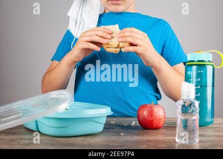 Öffentliche Schulen werden in den USA nach der virtuellen Ausbildung aufgrund der COVID 19 Pandemie wieder eröffnet. Ein kaukasischer Grundschüler isst sein Sandwich al Stockfoto