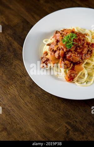 Hausgemachte leckere italienische Spaghetti mit Bolognese Fleischsoße und Petersilie Oben in weißem Teller auf Holztisch Stockfoto