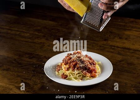 Der Koch reibe Parmesankäse auf Spaghetti Bolognese Weißes Gericht am Tisch Stockfoto