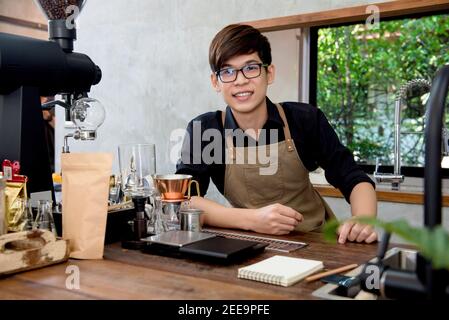 Junger asiatischer Unternehmer sitzt am Tresen in seinem eigenen Kaffee Kaufen Stockfoto