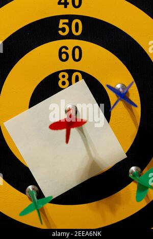 Eine Dartscheibe mit mehreren Pfeilen. Der rote Pfeil trifft das Bullseye. Unter dem Gewinnerpfeil befindet sich ein leeres Papier (Haftnotiz). Ein anpassbares Bild Stockfoto
