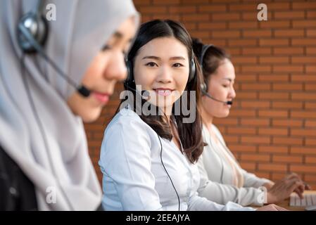 Gemischtes asiatisches Frauenteam, muslimische Chinesen und Japaner, die im Call Center als Kundendienstmitarbeiter arbeiten Stockfoto