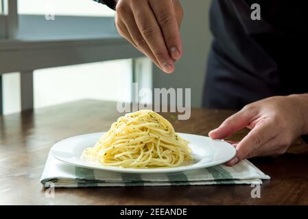 Küchenchef würzt italienische Spaghetti mit gemahlener Petersilie auf weißem Gericht Auf Kücheninsel Stockfoto