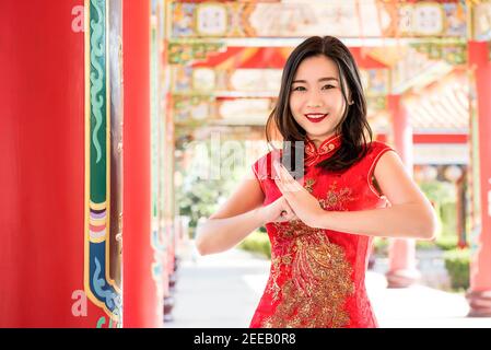 Lächelnde asiatische Frau in traditionellen roten Cheongsam Qipao Kleid machen Gruß Stockfoto