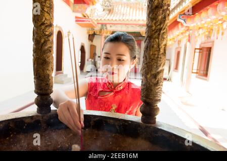 Asiatische Frau in roten Qipao Kleid beten mit Räucherstäbchen Während der chinesischen oder Lunar Neujahr im Tempel Stockfoto