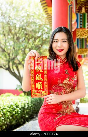 Lächelnde asiatische Frau in traditionellen roten Cheongsam Qipao Kleid zeigt Chinesisches Neujahrsgruß-Textschild sagte alles wird sein Gut Stockfoto