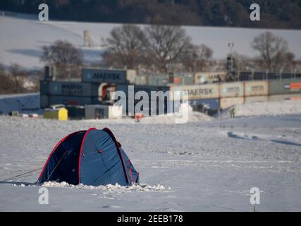 Dannenrod, Deutschland. Februar 2021, 14th. Nur ein Zelt der Autobahngegner steht auf einem verschneiten Feld vor dem Maschinenlager der Baufirmen, geschützt durch Container und NATO-Draht. (Zur 'Übergabe der freigetraegten Flächen an die Baufirma steht bevor') Quelle: Boris Roessler/dpa/Alamy Live News Stockfoto