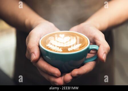 Barista Hände halten eine Tasse Kaffee präsentiert schöne Rosetta Latte Art Muster auf der Oberfläche Stockfoto
