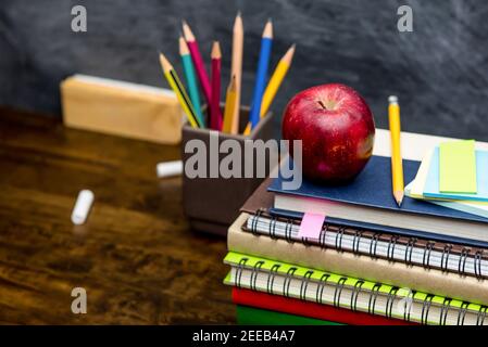 Stapel von bunten Büchern, Schreibwaren und Bildungsmaterialien auf Holztisch im Klassenzimmer mit Tafel im Hintergrund Stockfoto