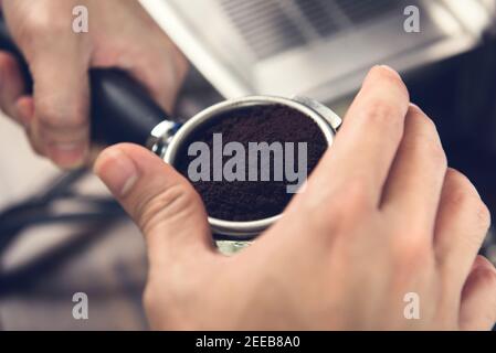 Die Hände des Barista halten den mit gemahlenem Kaffee gefüllten Portafilter, der für die Zubereitung mit der Maschine vorbereitet wird Stockfoto