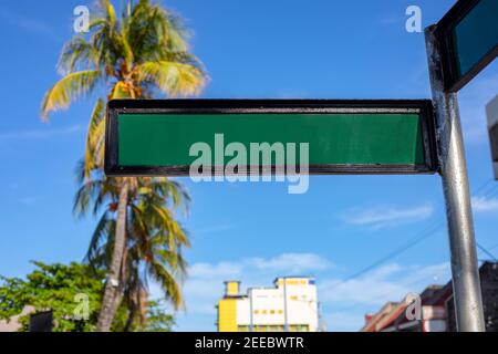 Leere Straßenschild auf sonnigen Stadtlandschaft mit Palmen und gelben Gebäude. Grünes Metallschild an der Säule. Südstadt verschwommen Landschaft auf b Stockfoto