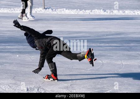 Junge in schwarzer Winterkleidung und bunten Schlittschuhen rutscht, verlor sein Gleichgewicht und fällt auf das Eis, die Arme ausgestreckt, um den Fall zu fangen Stockfoto