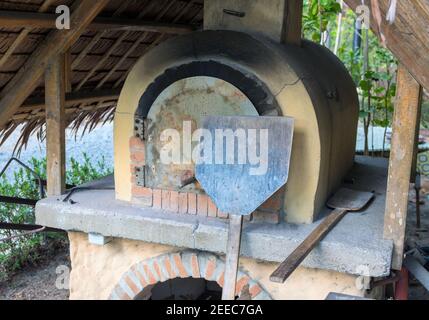 Alter Ofen mit Holzbackwerkzeugen. Pizza und Brot Kochen im Holzofen. Keramik-Steinofen im Vintage-Stil. Ländliche Bäckerei. Authentische Handwerkskunst Stockfoto