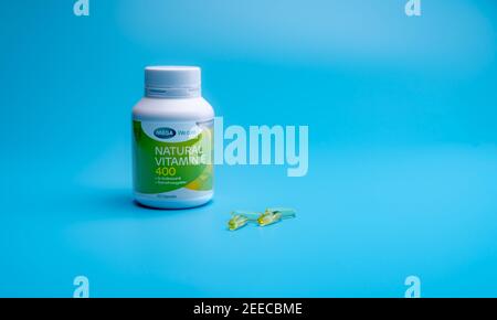 CHONBURI, THAILAND-JANUARY 31, 2021 : Mega We care Natural Vitamin E 400 IU in PP-Plastikflasche und vier weiche Gelatine Kapsel auf blauem Hintergrund. Stockfoto