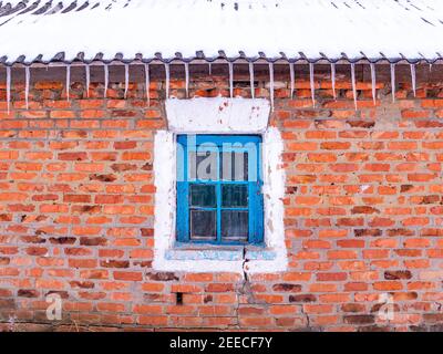 Eiszapfen von gefrorenem Wasser auf dem Dach des Hauses über dem Fenster. Schnee schmilzt. Winter. Frühlingstropfen. Eiszapfen. Gefrorenes Wasser. Ziegelwand. Frostiger Fr Stockfoto