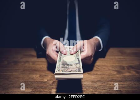 Anonymer Geschäftsmann heimlich verschenken Geld, japanische Yen Währung, in privaten dunklen Raum - Darlehen, Betrug und Bestechung Konzepte Stockfoto