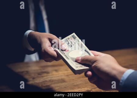 Geschäftsmann heimlich verschenken Geld, japanische Yen Währung, zu seinem Partner in privaten dunklen Raum nach einem Deal-Darlehen, Bestechung und Korruption c Stockfoto
