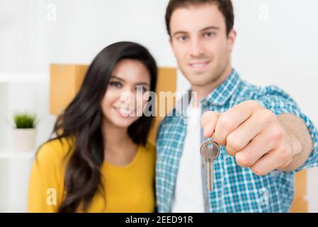 Interracial Paar zeigt den Schlüssel des neuen Hauses mit beweglichen Boxen im Rücken. Stockfoto