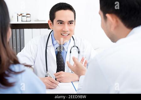 Schöner männlicher Arzt Beratung ein Paar über Unfruchtbarkeit in seinem Arztpraxis Stockfoto