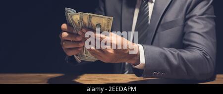 Ein Geschäftsmann, der Geld zählt, US-Dollar-Scheine, in dunklen privaten Raum - Darlehen, Zahlung und Bestechung Konzept, Panorama-Banner Stockfoto