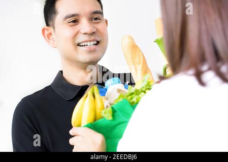 Asian Lebensmittelgeschäft Delivey Mann trägt ein schwarzes Polo-Shirt liefern Essen für eine Frau zu Hause Stockfoto