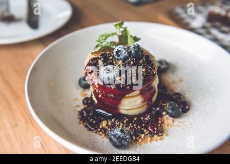 Schöne appetitliche Stapel von flauschigen Pfannkuchen mit frischen Heidelbeeren, Sirup und gemahlenen Keks in weißen Teller gekrönt Stockfoto