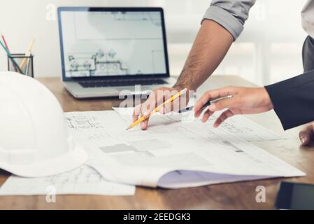 Architekten- oder Ingenieurteam, das ein Projektdesign anhand von Bauplänen und einem Laptop-Computer im Büro diskutiert, bevor es die Baustelle besucht. Stockfoto