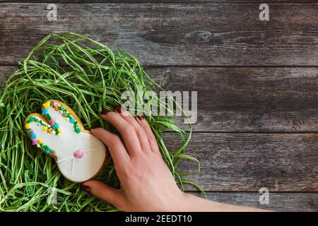 Womans Hand nimmt eine der bunten ostereier Cookies aus Nest auf hellem Holzhintergrund. Flach liegend, Draufsicht Stockfoto