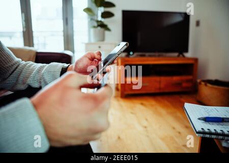 Nahaufnahme gemischter Rennbusiness Mann auf Couch sitzend, der tippt Auf dem Smartphone im Wohnzimmer Stockfoto