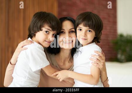 Porträt von zwei lateinischen Kindern, kleinen Zwillingsjungen lächeln an der Kamera und umarmen ihre Mutter, verbringen Zeit zusammen zu Hause. Familie, Kindheitskonzept Stockfoto