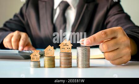 Holzhausmodell auf Münzen und Menschenhänden, Immobilieninvestitionsideen und Finanztransaktionen. Stockfoto