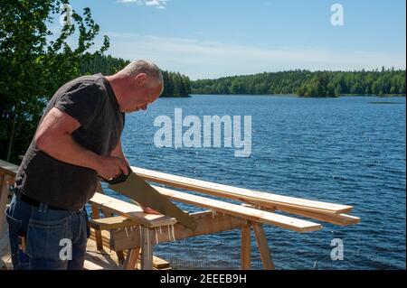 Bau eines Gästehauses am See. Ein Zimmermann sägt Bretter. Stockfoto