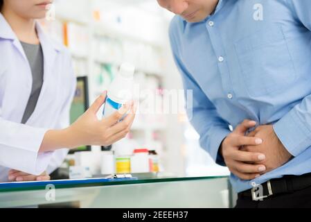 Männlicher Patient mit Magenschmerzen, Beratung mit Apotheker in der Apotheke Stockfoto