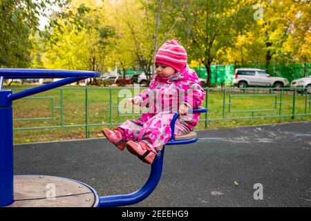 Kleines Kleinkind in warmen Winteroveralls spielt auf dem Spielplatz. Weicher Fokus Stockfoto