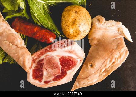 Zutaten des galizischen Eintopfrezeptes während des Karnevals bestehend aus Kartoffeln, Schweineschenkel, lacon, geräuchertem Ohr, Chorizo ​​and Rübengemüse auf Schiefer-tra Stockfoto