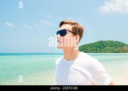 Männlicher Tourist mit Sonnenbrillen, der im Sommer am Strand steht Stockfoto