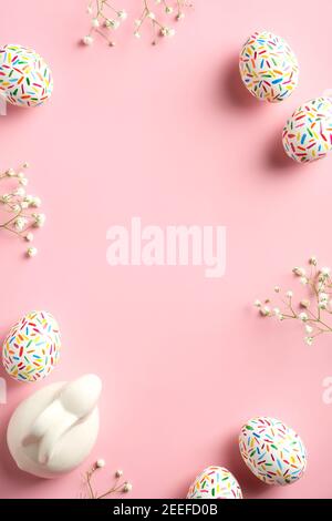 Frohe Ostern Karte. Rahmen aus bunt gesprenkelten Ostereiern, Osterhasen und Frühlingsblumen auf rosa Hintergrund. Vertikales Banner-Mockup für soziale Medien Stockfoto