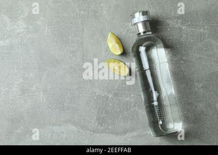 Flasche Wodka und Limettenscheiben auf grauem Hintergrund Stockfoto
